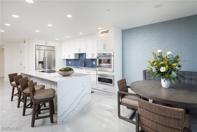 kitchen featuring a center island, sink, appliances with stainless steel finishes, light stone counters, and white cabinetry