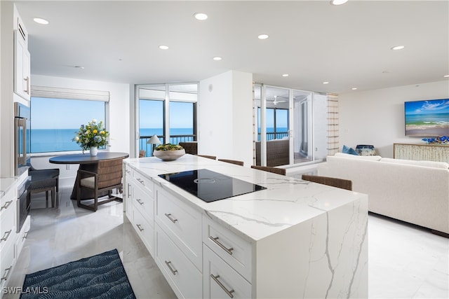 kitchen with white cabinetry, light stone countertops, black electric stovetop, and a kitchen island