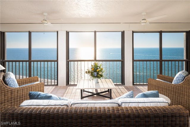 sunroom with ceiling fan and a water view