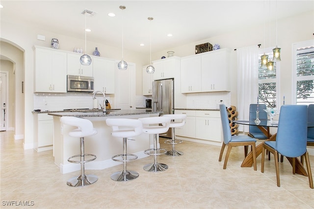 kitchen with white cabinets, hanging light fixtures, an island with sink, tasteful backsplash, and stainless steel appliances