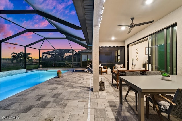 pool at dusk featuring glass enclosure, ceiling fan, a patio, and an outdoor living space