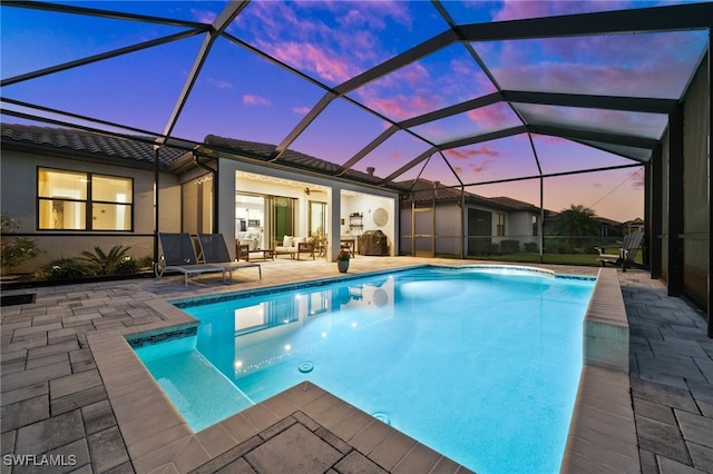 pool at dusk with glass enclosure, ceiling fan, outdoor lounge area, and a patio