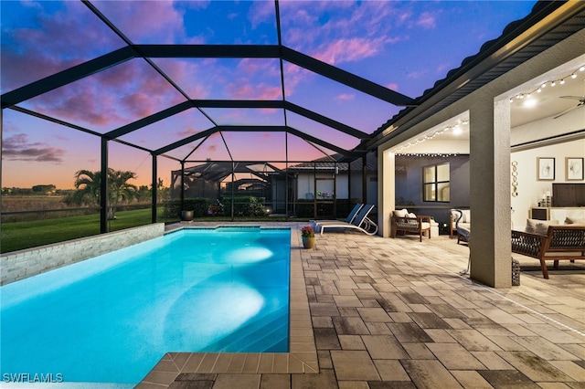 pool at dusk featuring glass enclosure, a patio area, and an outdoor hangout area