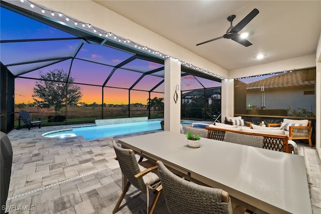 pool at dusk featuring outdoor lounge area, ceiling fan, a lanai, an in ground hot tub, and a patio