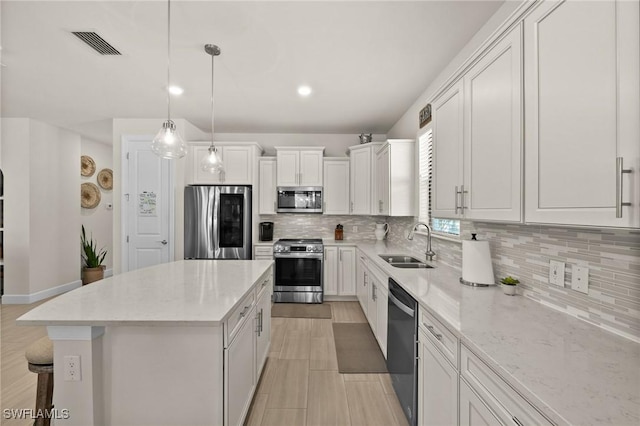 kitchen with pendant lighting, a center island, sink, appliances with stainless steel finishes, and white cabinetry