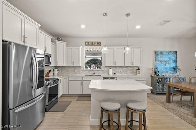 kitchen with appliances with stainless steel finishes, a breakfast bar, pendant lighting, white cabinetry, and a kitchen island