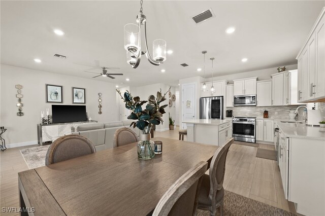 dining area with ceiling fan with notable chandelier and sink