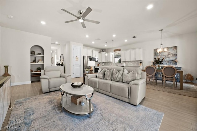 living room featuring ceiling fan with notable chandelier, light hardwood / wood-style floors, and built in features