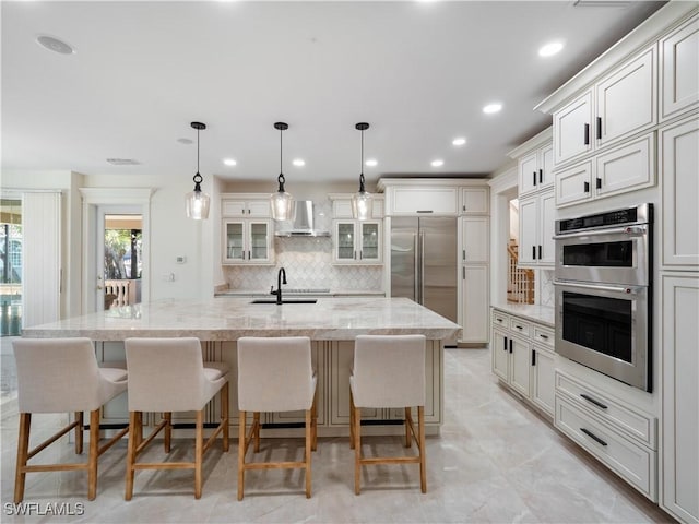 kitchen with a large island with sink, light stone counters, appliances with stainless steel finishes, and sink