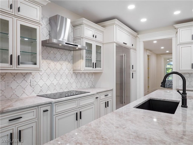 kitchen with light stone countertops, black electric cooktop, sink, wall chimney range hood, and white cabinets