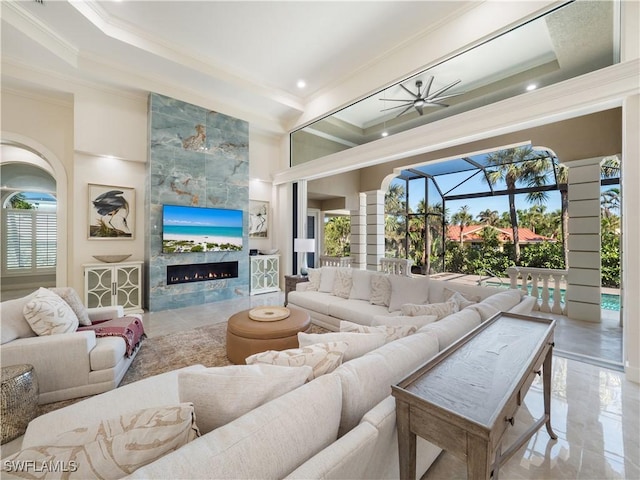 living room featuring ceiling fan, a fireplace, a towering ceiling, and ornamental molding