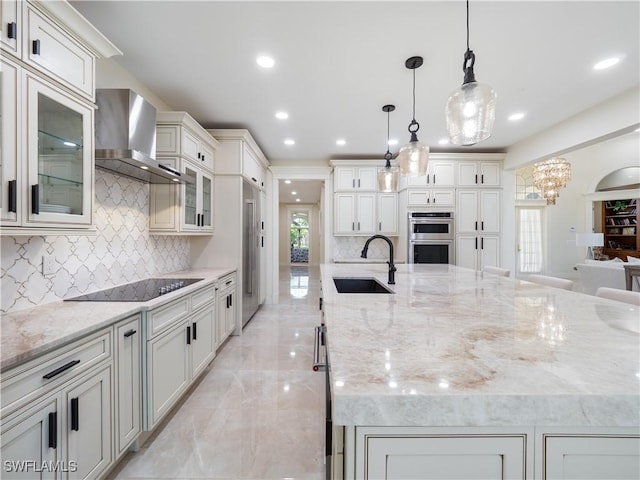 kitchen featuring double oven, sink, wall chimney range hood, pendant lighting, and a large island