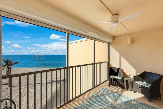 sunroom with ceiling fan, a water view, and a beach view