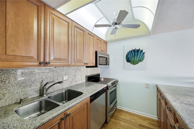 kitchen featuring appliances with stainless steel finishes, light wood-type flooring, backsplash, light stone counters, and sink