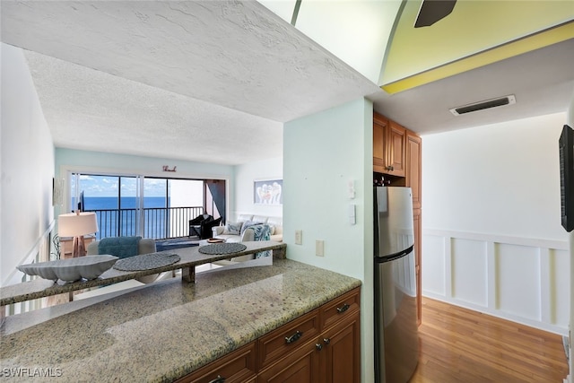 kitchen featuring stainless steel refrigerator, light stone counters, light hardwood / wood-style floors, a textured ceiling, and a water view