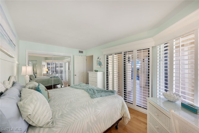 bedroom with access to exterior, light wood-type flooring, a closet, and multiple windows