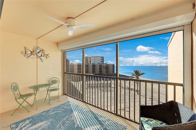 sunroom with ceiling fan, a water view, and a view of the beach