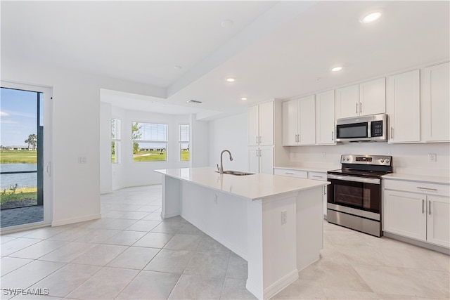 kitchen featuring stainless steel appliances, sink, a water view, a center island with sink, and white cabinetry