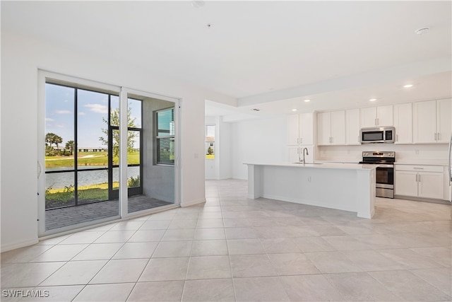 kitchen with a kitchen island with sink, white cabinets, a water view, sink, and appliances with stainless steel finishes