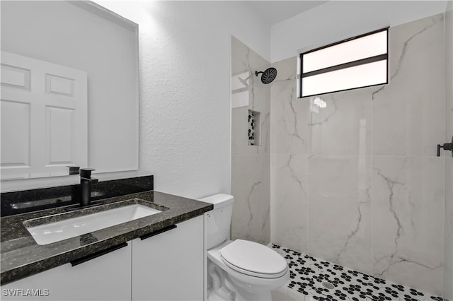 bathroom with a tile shower, vanity, and toilet