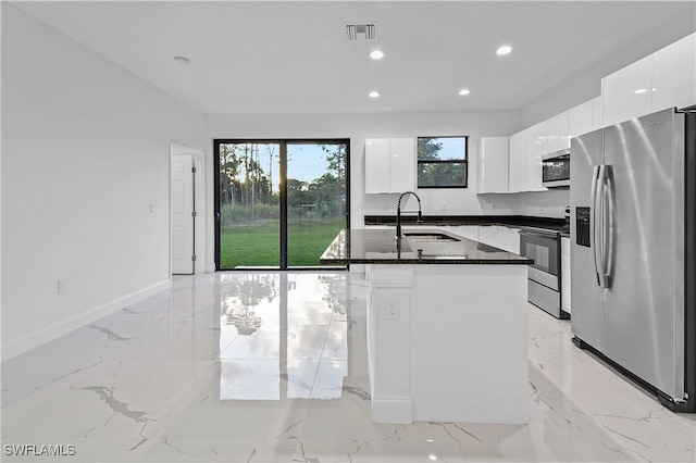 kitchen featuring dark stone counters, stainless steel appliances, a kitchen island with sink, sink, and white cabinets