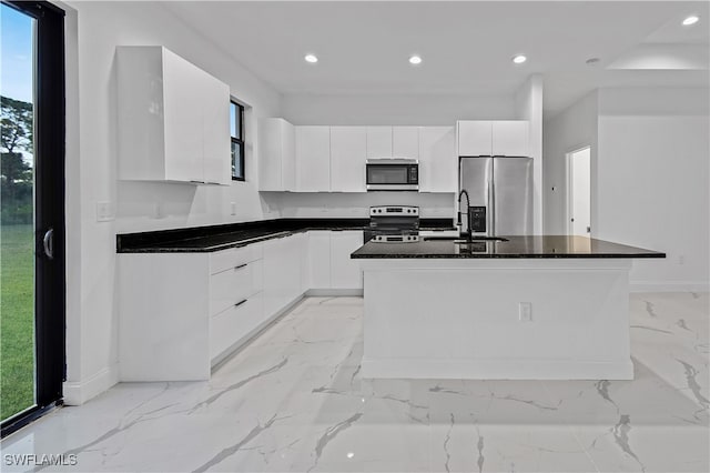 kitchen with white cabinets, sink, dark stone countertops, an island with sink, and stainless steel appliances