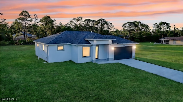 back house at dusk with a lawn and a garage