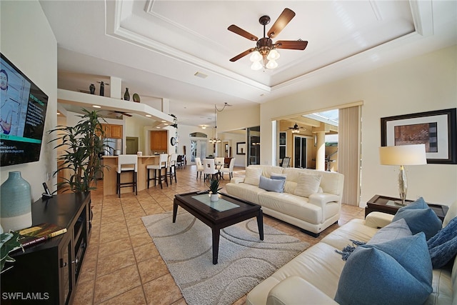 tiled living room with ceiling fan and a tray ceiling