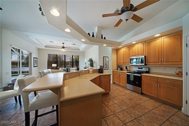 kitchen with an island with sink, appliances with stainless steel finishes, a raised ceiling, a breakfast bar, and sink