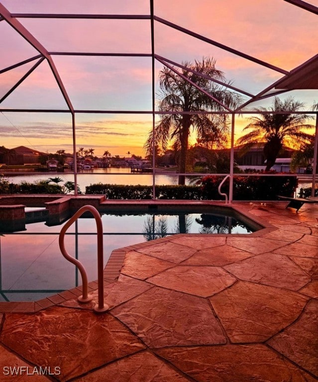 pool at dusk with a lanai, a water view, and a patio