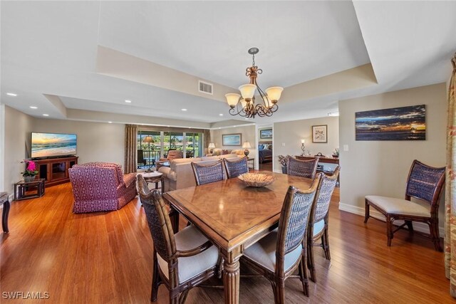 dining room with a chandelier, hardwood / wood-style flooring, and a raised ceiling