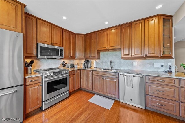 kitchen featuring light stone countertops, sink, tasteful backsplash, appliances with stainless steel finishes, and light wood-type flooring