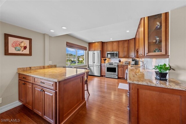 kitchen with kitchen peninsula, light wood-type flooring, light stone counters, a breakfast bar, and stainless steel appliances