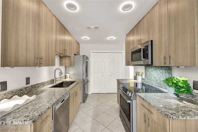 kitchen with appliances with stainless steel finishes, light stone counters, a textured ceiling, sink, and light tile patterned floors