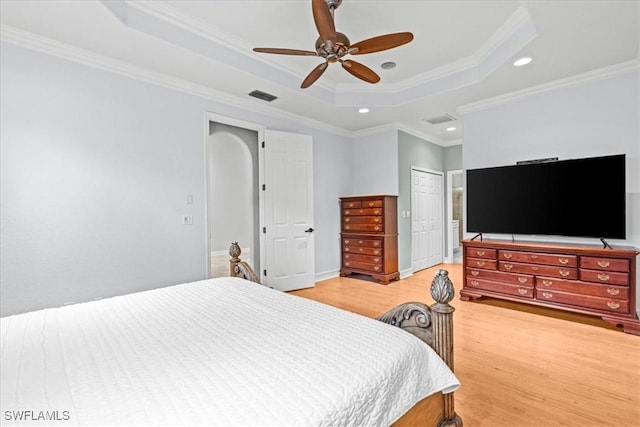 bedroom with hardwood / wood-style flooring, a closet, ornamental molding, a raised ceiling, and ceiling fan