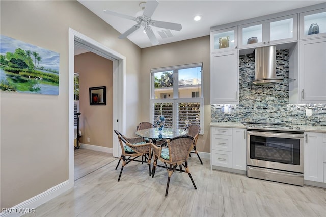 kitchen with backsplash, light hardwood / wood-style flooring, electric range, wall chimney exhaust hood, and white cabinetry