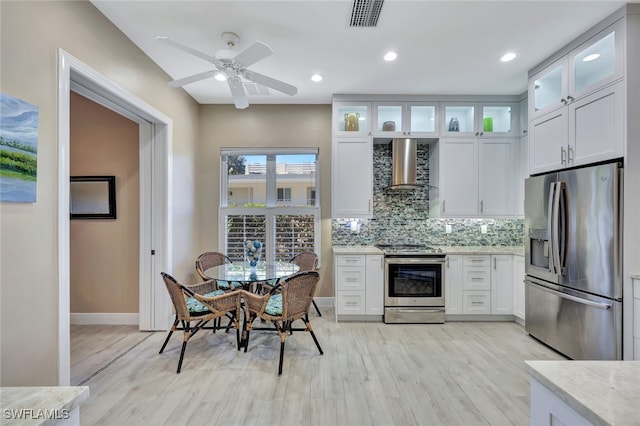 kitchen featuring appliances with stainless steel finishes, light hardwood / wood-style flooring, white cabinetry, and wall chimney exhaust hood