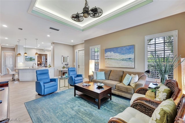 living room with light hardwood / wood-style floors, ceiling fan, ornamental molding, and a tray ceiling