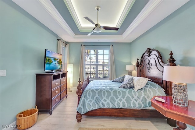 bedroom with ceiling fan, a raised ceiling, ornamental molding, and light hardwood / wood-style flooring