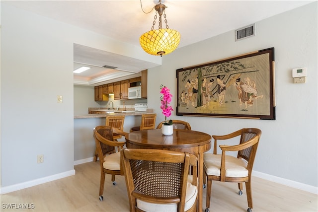 dining space featuring a raised ceiling and light hardwood / wood-style flooring