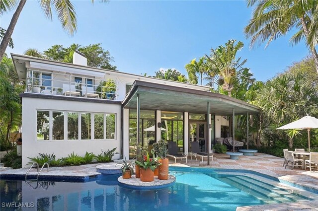 rear view of house with a balcony, stucco siding, an outdoor pool, a chimney, and a patio area