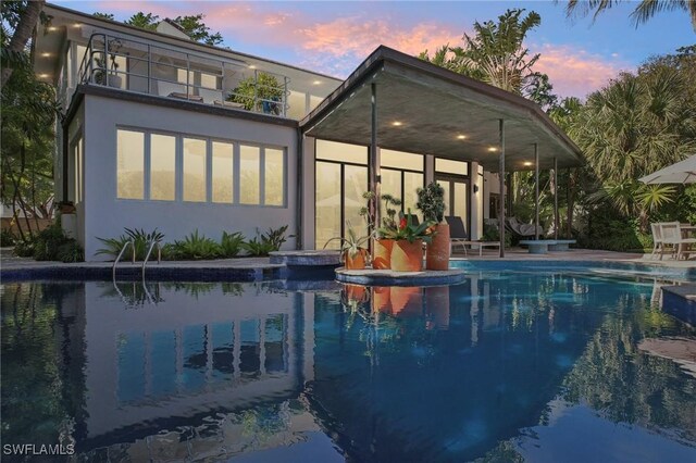 back of house with a patio area, an outdoor pool, a balcony, and stucco siding