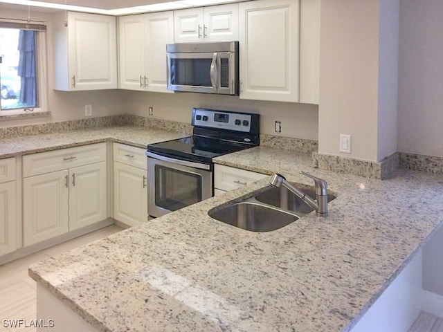 kitchen with kitchen peninsula, light stone counters, stainless steel appliances, sink, and white cabinets