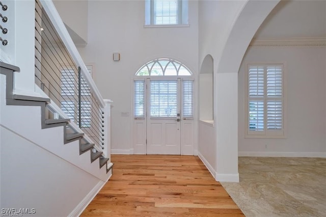 entrance foyer with light hardwood / wood-style flooring, a high ceiling, and ornamental molding