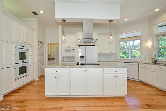 kitchen with white appliances, island range hood, white cabinets, light hardwood / wood-style floors, and hanging light fixtures