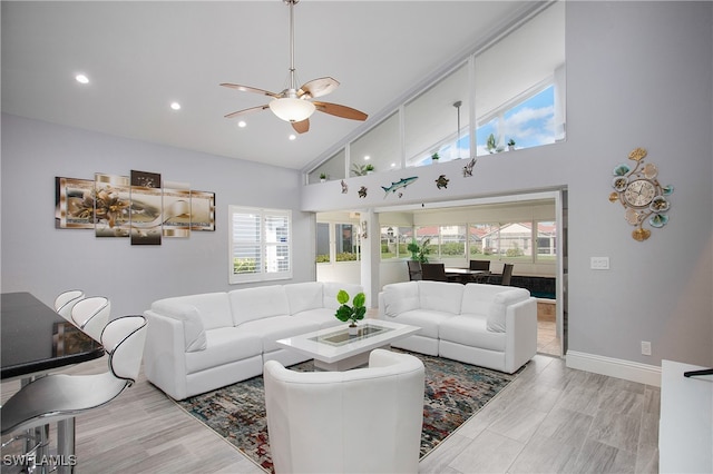 living room with ceiling fan, plenty of natural light, high vaulted ceiling, and light wood-type flooring