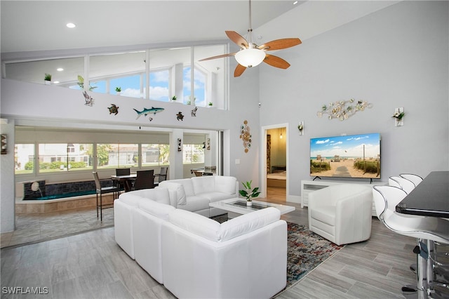 living room with ceiling fan, high vaulted ceiling, a healthy amount of sunlight, and light wood-type flooring