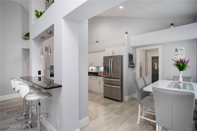 159 Lady Palm Dr, Naples, FL 34104 - kitchen with stainless steel fridge, high vaulted ceiling, a kitchen bar, white cabinetry, and dark countertops