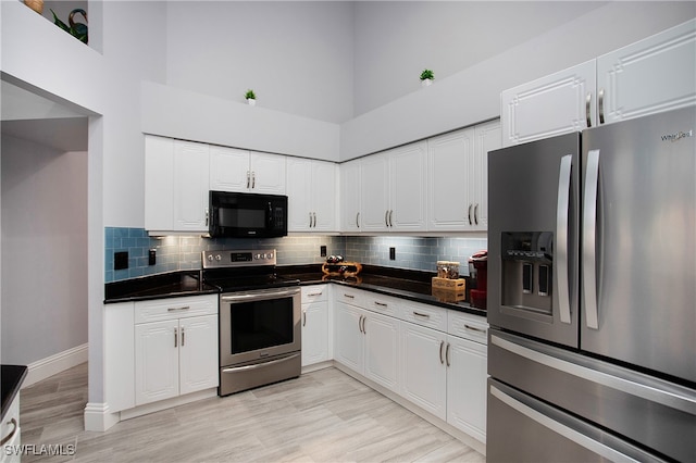 kitchen with white cabinets, a towering ceiling, and stainless steel appliances