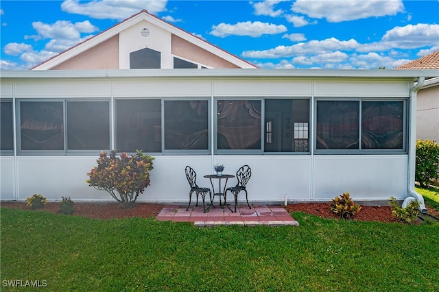 rear view of property with a lawn, a patio area, and a sunroom